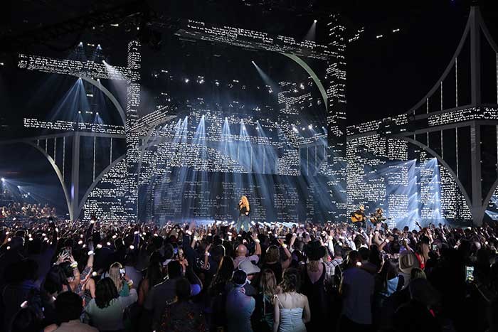a stage featuring projected text on a variety of architecture. white beams of light cut through the space at different angles