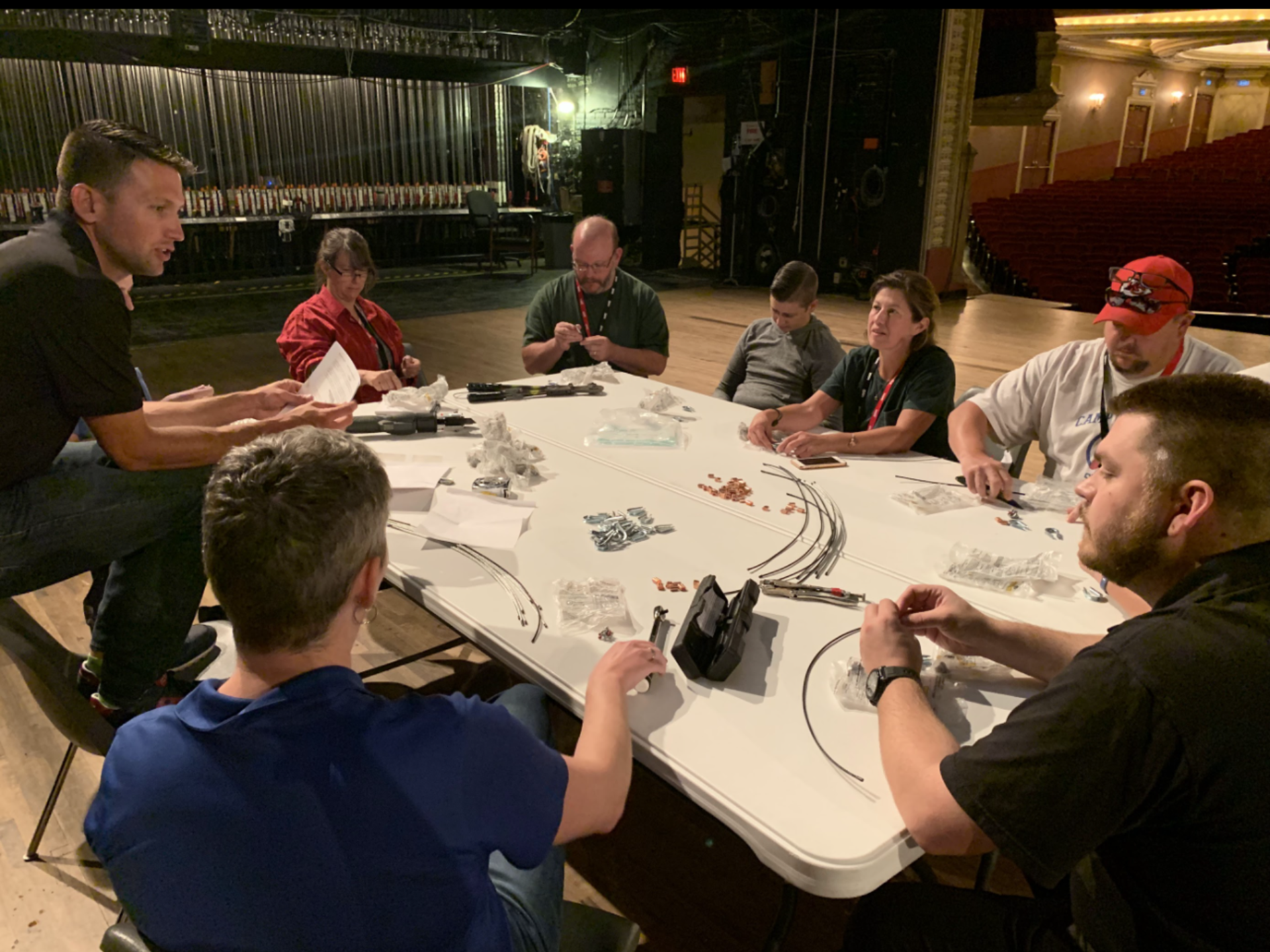 Glerum Masterclass participants sit with trainer at table on a stage learning rigging basics