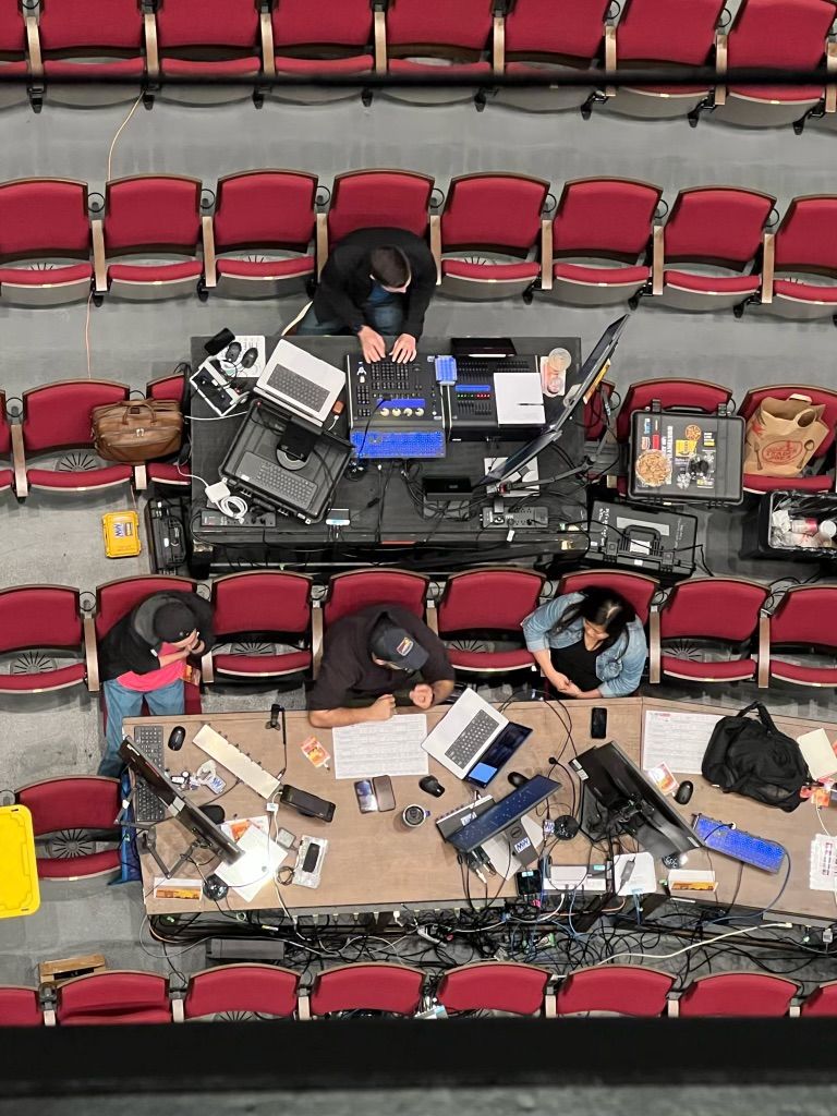 Birds eye view of people sitting in a theatre working at various tables with their laptops and lighting consoles