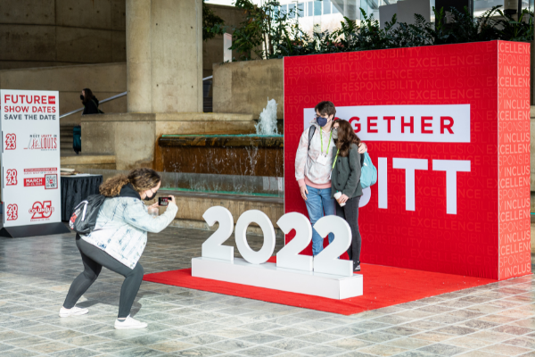 A person taking a photo for others at the USITT 2022 step and repeat in the registration lobby
