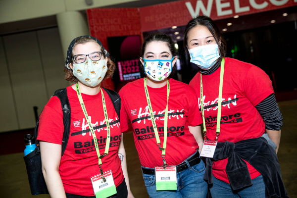 3 individuals standing in lobby with student assistant shirts