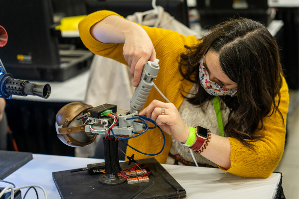 An individual using a hot glue gun on an electronic prop