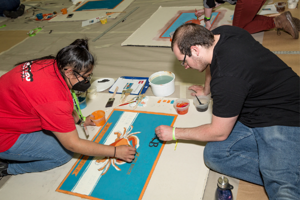 Two individuals painting on the floor during Paint Lab