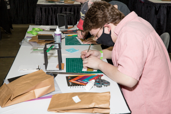 A person using an exacto knife to construct a mini set design model during a lab