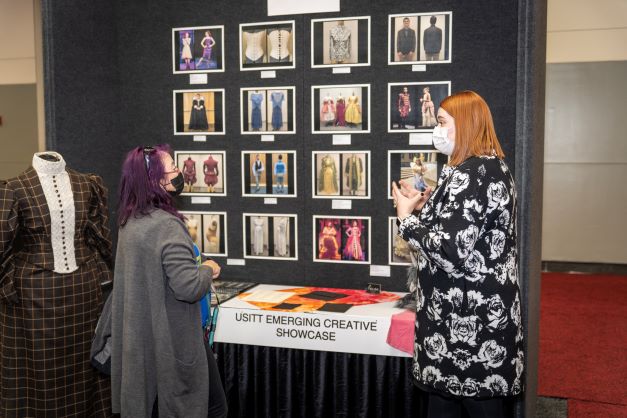 a perosn showing their work to an attendee at their emerging creatives showcase booth on the expo floor