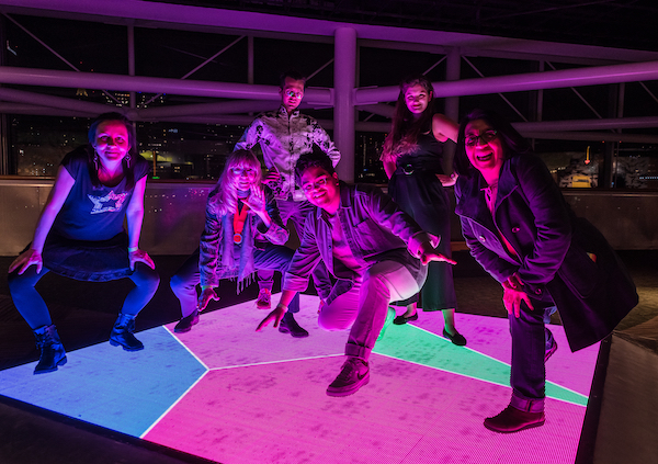 a group of people standing under colorful lights posing at the Friday night reception