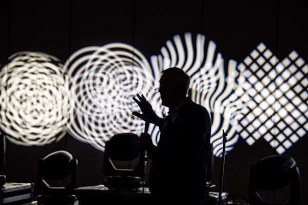 ken billington giving a lighting demonstration on the expo floor with black and white swirl lighting behind him